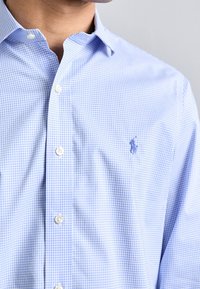 Camicia in cotone azzurro chiaro a quadri con colletto button-down, bottoni bianchi e un piccolo logo ricamato sul petto.
