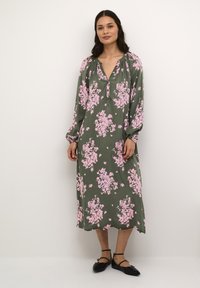Rochie cu mânecă lungă, de culoare verde măslinie, cu motive florale roz, decolteu în V și mâneci bufante, având o croială lejeră care ajunge până la jumătatea gambei.