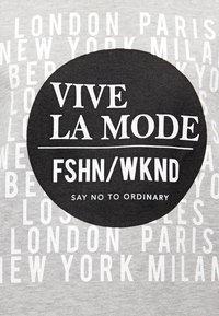 Camiseta gris con nombres de ciudades en blanco y un gráfico circular negro con "VIVE LA MODE FSHN/WKND DICE NO A LO ORDINARIO" en letras negritas.