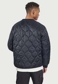 Chaqueta bomber acolchada en navy hecha de material sintético suave, con un patrón elevado, puños acanalados y un corte holgado.