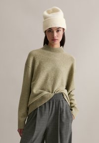 Pull en laine vert clair avec un col montant et un ourlet côtelé, associé à un pantalon à motif écossais gris avec une coupe décontractée et une taille élastique.