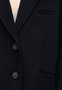 Tume villane bleiser, millel on sisselõigatud krae, kaks esimest nuppu ja küljetaskute detailid, sileda tekstuuriga.