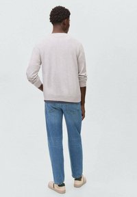 Suéter gris claro con cuello redondo, combinado con jeans azules y zapatillas beige. Muestra un ajuste casual y relajado con puños acanalados.