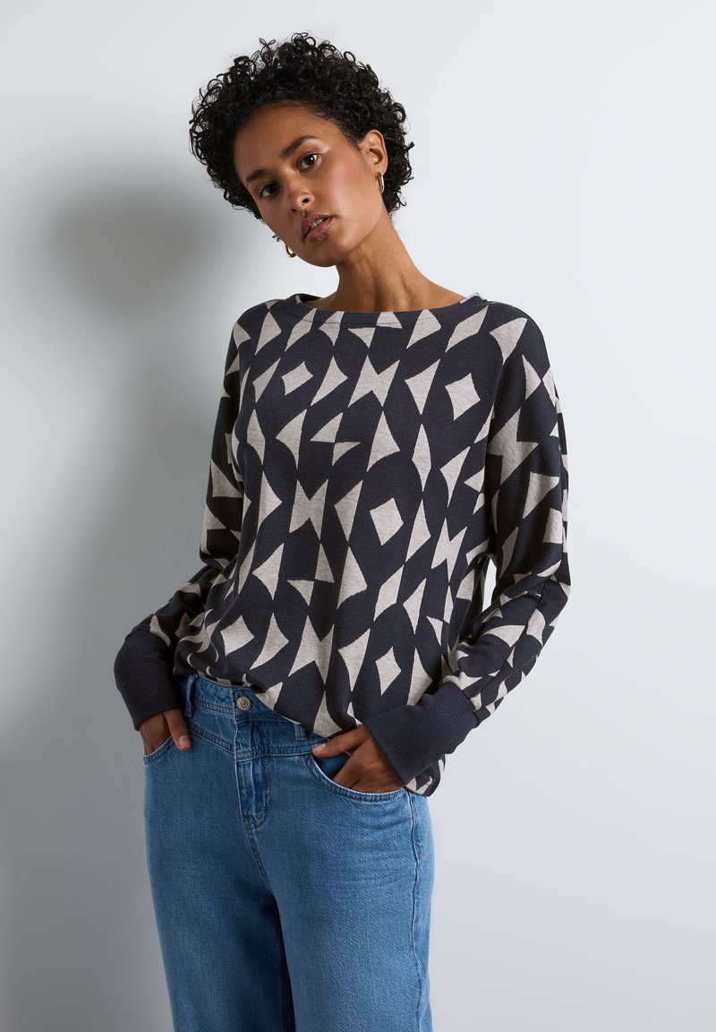 Námořnický a krémový vzorovaný svetr s širokým výstřihem a dlouhými rukávy, doplněný světle modrými džíny. Měkká textura a uvolněný střih.