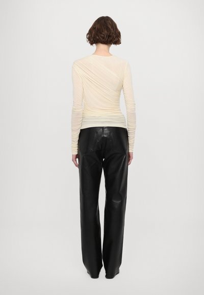 Blusa de manga larga color beige claro con textura fruncida, combinada con pantalones de cuero negros de tiro alto, con piernas rectas y bolsillos traseros.