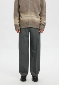 Grå vide bukser kombinert med en beige og brun gradient strikket genser med glidelås. Stoffet ser mykt ut med ribbekant nederst. Svarte sko fullfører antrekket.