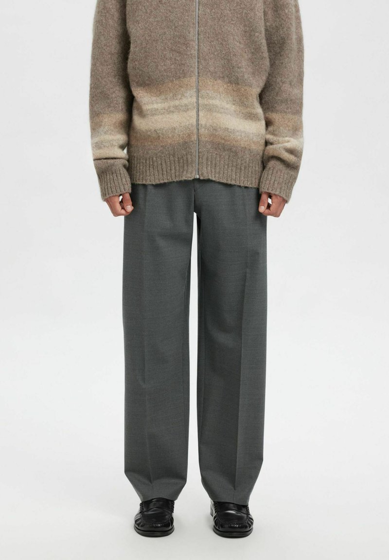 Grå vide bukser kombinert med en beige og brun gradient strikket genser med glidelås. Stoffet ser mykt ut med ribbekant nederst. Svarte sko fullfører antrekket.