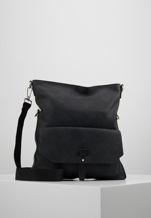 Zwarte schoudertas met brede, gestructureerde riem, voorklep met drukknoop en zilverkleurige hardware op een wit voetstuk.