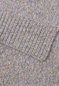 Close-up van twee gebreide sokken in beige en lichtblauwe garen, met ribbelboord en gestructureerde steken.