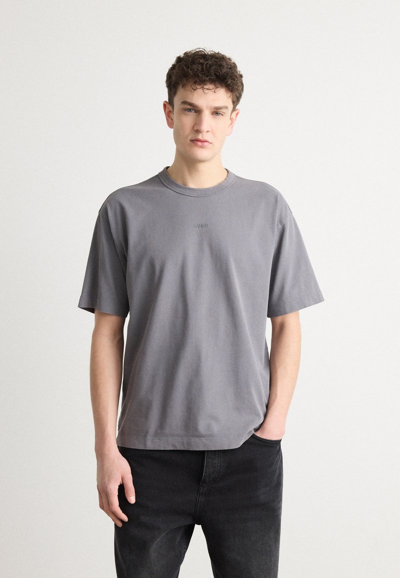 T-shirt en coton gris avec des manches courtes, un col rond et un logo en relief sur la poitrine. Associé à un jean noir, au toucher lisse.