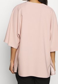 Vaaleanpunainen oversized-paita, joka on valmistettu pehmeästä kankaasta. Paita sisältää leveät hihat, pyöreän pääntien ja sivureiät lisäliikkuvuuden takaamiseksi.