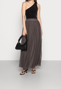 Schwarzer Ein-Schulter-Body kombiniert mit einem fließenden, grauen Maxirock. Schwarze Handtasche mit gedrehtem Griff und schwarze Sandalen mit Absatz.