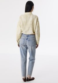 Lichtgele linnen shirt, losse pasvorm, achteraanzicht; gecombineerd met lichtblauwe hoge taillejeans, gescheurde zoom, en bruine platte schoenen.