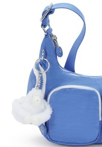 Blaue Stofftasche mit geschwungener Form, ausgestattet mit einem weißen Kunstfell-Anhänger und silbernem Zubehör. Die Tasche hat kontrastierende weiße Nähte und Taschen.