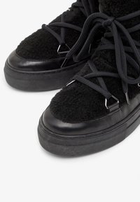 Sneaker neri con tomaia in tessuto soffice e dettagli in pelle liscia. Suola in gomma spessa con punta arrotondata e un sistema di allacciatura elaborato.
