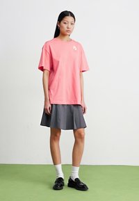 Roze katoenen t-shirt met korte mouwen en een kleine afbeelding op de borst, gecombineerd met een grijze plakrok, witte sokken en zwarte schoenen.