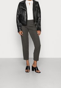 Veste de motard en cuir noir sur un haut blanc à col en trou de serrure, associée à un pantalon tapered vert olive et des sandales à talons blocs noires.