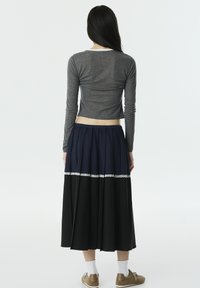 Graues Langarmoberteil, kurzes Design. Fließender, knielanger Rock mit oben navyblauem und unten schwarzem Abschnitt sowie Spitzenbesatz an der Taille.