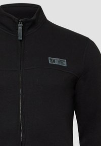 Zwarte zip-up jas van zachte stof, met een hoge kraag, een voorste ritssluiting en een klein logopatch bij de schouder.