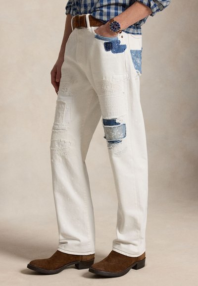 Άνδρας που φοράει λευκά σκισμένα τζιν με μπλε τζιν μπαλώματα, καφέ ζώνη, μπλε πουκάμισο με καρό σχέδιο, καφέ σουέτ μπότες και ρολόι χειρός.