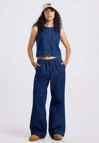 Denim kaksiosainen asu, johon kuuluu lyhythihainen toppi ja leveälahkeiset housut. Tumansini väri, joustava vyötärö ja rento fit.