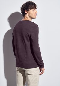Long-sleeve shirt in dark purple textured fabric, featuring a crew neck and straight cut. Paired with light beige pants. Back view.