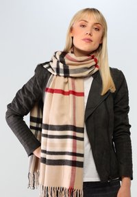 Beige plaid tørklæde med sorte og røde striber, frynser i kanten, lavet af blødt stof, båret over en sort læderr jakke.