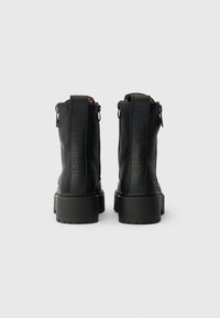 Črne gležnjarje iz teksturirane usnje s debelim podplatom, ki imajo zadaj zadrgo in embosirano blagovno znamko.