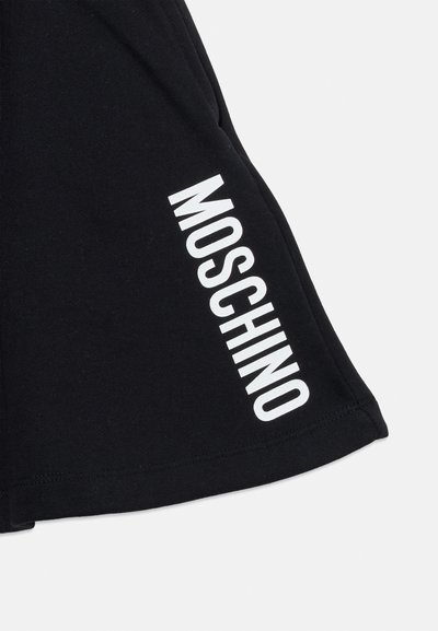 Tissu noir avec texte "MOSCHINO" blanc imprimé en diagonale près de l'ourlet, montrant des coutures nettes le long du bord.