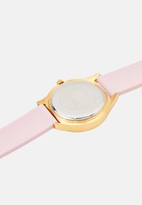 Kuldtooni randmevaatja tagakülg, millel on hõbedane seljaosa ja helesinine silikoonist rihm valgel taustal.