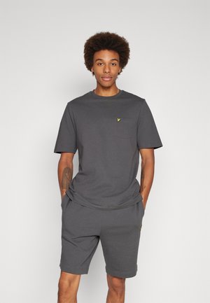 T-shirt grigia in cotone con collo rotondo e maniche corte, caratterizzata da un piccolo logo giallo sul taschino sinistro. Abbinata a pantaloni corti grigi coordinati.