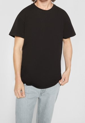 Czarna bawełniana koszulka z okrągłym dekoltem, krótkimi rękawami i luźnym krojem; gładka faktura i zaokrąglony dół. W zestawieniu z jasnoniebieskimi dżinsami.