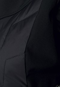 Czarna kurtka wykonana z mieszanki gładkiego i teksturowanego materiału, z pikowaną częścią i detalami szwów. Brak widocznych metalowych elementów lub wzorów.