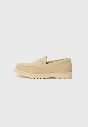 Beige suédist loafer ümarate varvastega, tikitud detailide ja tekstureeritud kummitaldaga. Lihtne jalga panna disain, millel on peen pealne aksent.