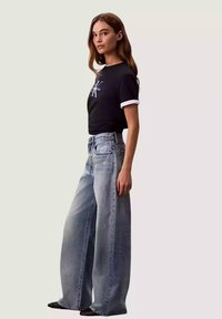 T-shirt nera corta con polsini bianchi e logo, abbinata a jeans azzurri a vita alta e gambe larghe. Tessuto in denim liscio, con pochissime abrasioni.