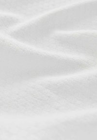 Tissu blanc texturé, présentant un subtil motif en diamant, avec des plis doux et une surface lisse, reflétant la lumière doucement.