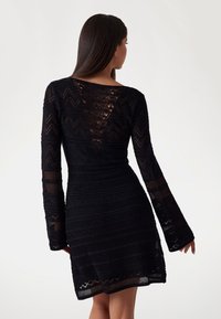 Abito nero a maglia con maniche lunghe, un motivo testurizzato a zigzag e un design a schiena a V. Lunghezza corta e silhouette aderente.
