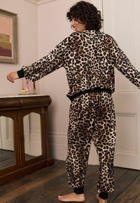 Súprava pohodlného oblečenia s leopardím vzorom vyrobená z mäkkej látky. Obsahuje uvoľnený strih, čierne rebrované manžety a elastický pás. Prevládajú zemské farby.