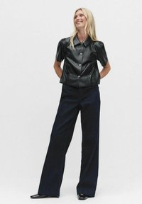 Zwart leren blouse met korte mouwen en knoopsluiting, gecombineerd met donkerblauwe wijde broek. Gladde textuur en gestructureerd ontwerp.