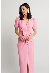 Różowa, dopasowana sukienka z bufkowymi rękawami, głębokim dekoltem w kształcie V i przednim detalem w postaci kokardy. Posiada rozcięcie do uda oraz gładką, miękką teksturę materiału.