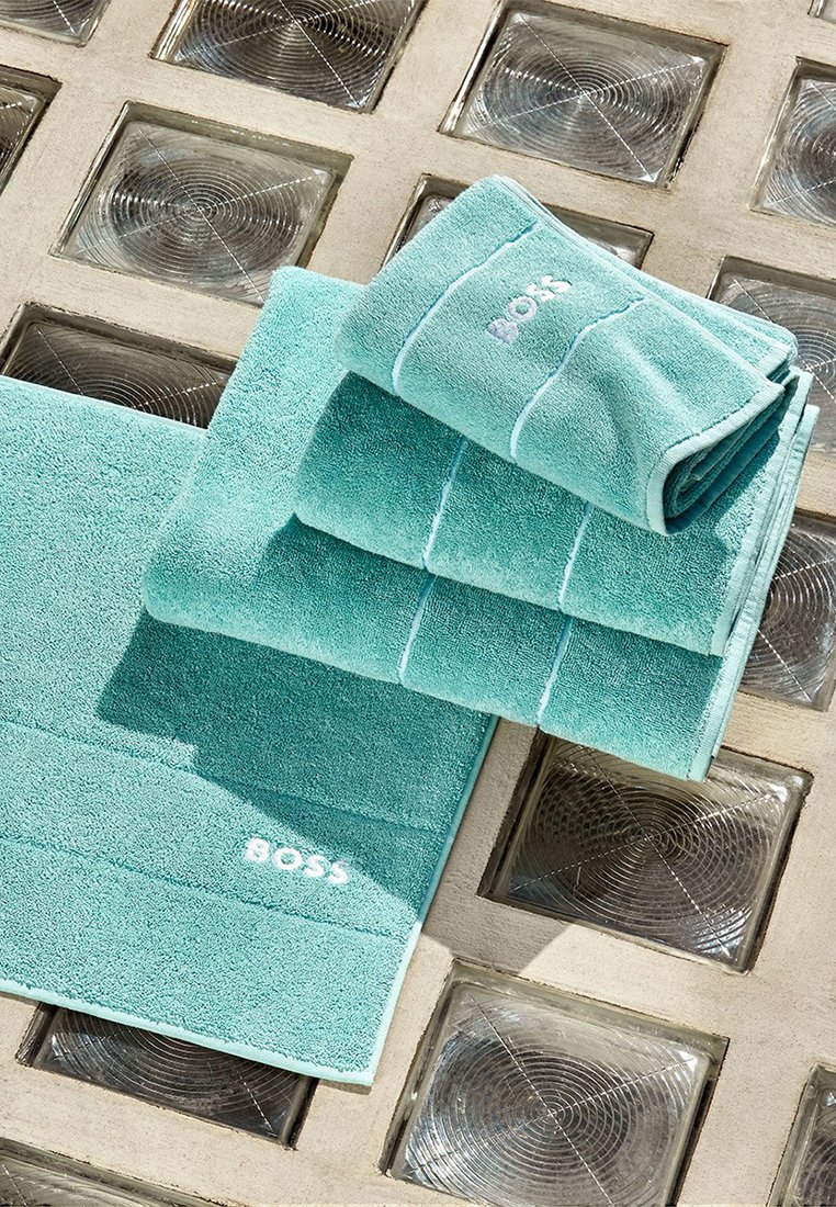 Türkisfarbene Baumwollhandtücher in verschiedenen Größen, mit weißen Streifen und "BOSS"-Logo. Weiche Textur, ordentlich gefaltet auf einer strukturierten Oberfläche.