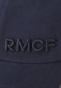 Námornícka čiapka z bavlny s textúrovaným povrchom, s vyšitým logom "RMCF" v tmavšej námorníckej modrej. Sklon je zakrivený, s jemnými detailmi prešívania.