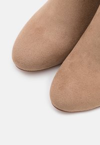 Botas de tobillo de ante beige con punta redonda, textura suave y un brillo sutil. Sin herrajes o acentos visibles.