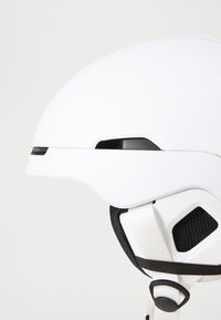 Casco di sicurezza bianco con finitura liscia, forma aerodinamica, cinturini neri regolabili e rete di ventilazione sui lati.