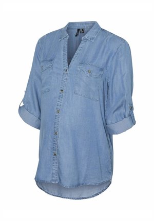 Lys blå denimskjorte med knaplukning fortil, opkrøllede ærmer, to brystlommer og en buet kant. Blød tekstur, afslappet design.