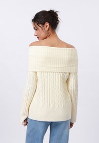 Off-white bezplecu džemperis ar ribotām aprocēm, ar pompu adījumu un brīvu piegriezumu. Kombinēts ar gaiši ziliem džinsiem.