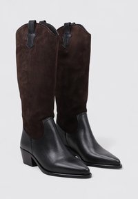 Parte inferior en cuero negro con un acabado texturizado, parte superior en ante marrón, puntera con forma puntiaguda y tacón bloque. Presenta acentos en contraste.