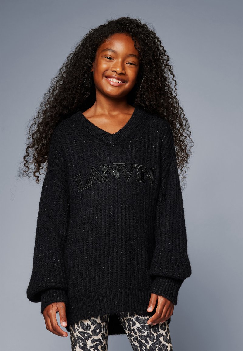 Black knitted sweater with a V-neck and long, loose sleeves, featuring raised "LANVIN" lettering on the front. Paired with leopard-print leggings.