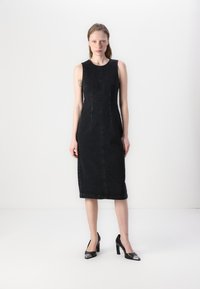 Black denim sleeveless dress with a fitted design, knee-length hem, vertical seams, and two inset pockets. Paired with black high-heeled shoes.