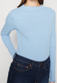 Hellblau gestreiftes Langarmoberteil mit einem gewellten runden Halsausschnitt und körperbetontem Schnitt, kombiniert mit dunkelblauen Denim-Jeans.